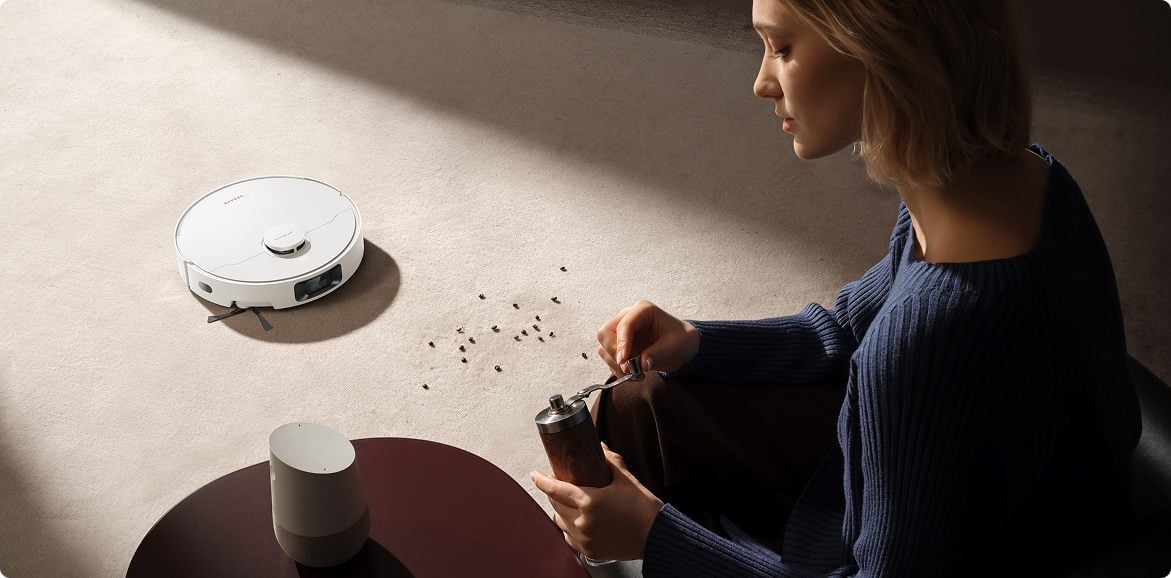 nő kávébabot szór ki, a háttérben a robot felporszívózza azokat